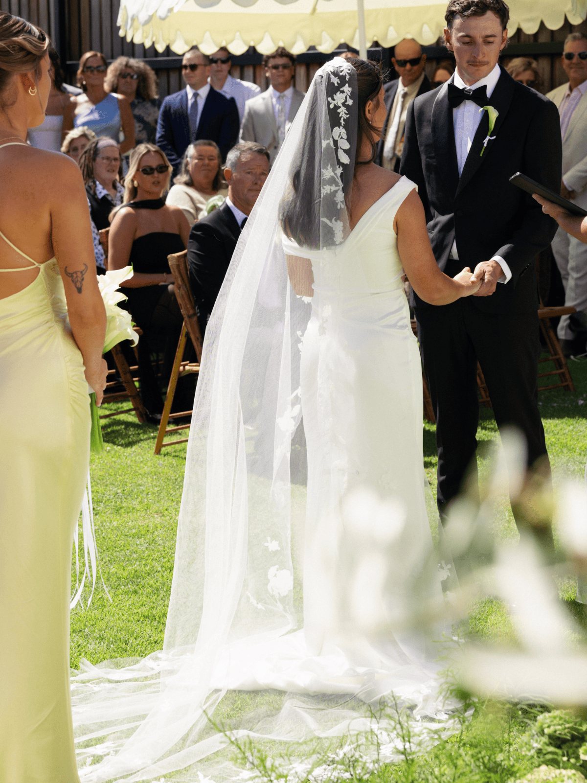 A bride with a long veil meeting her groom at the end of the lawn aisle