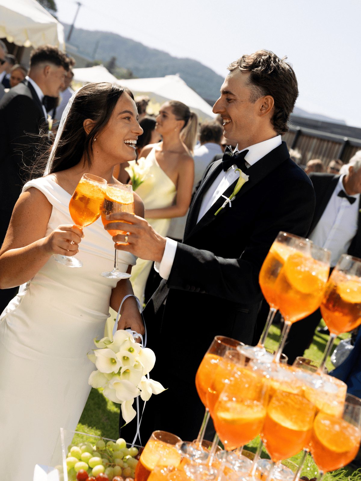 A couple toasting with spritz glasses beside a tower of orange drinks