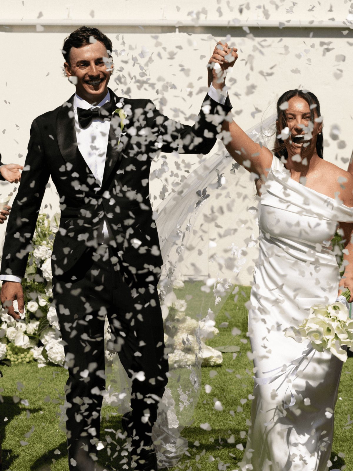 A groom punching the air as the couple walk out through confetti