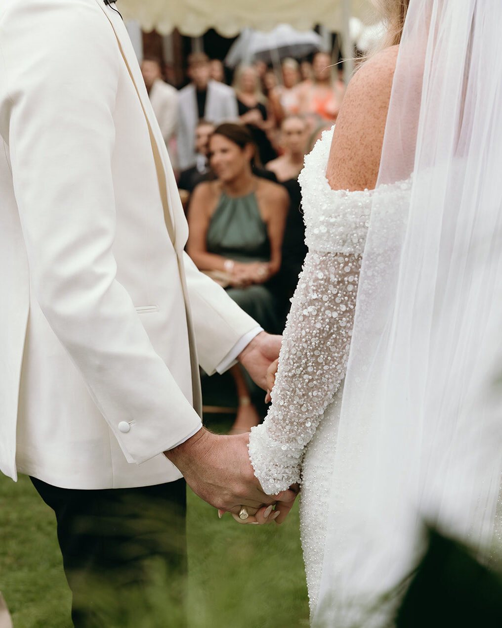 Bride and groom holding hands during the ceremony, guests behind