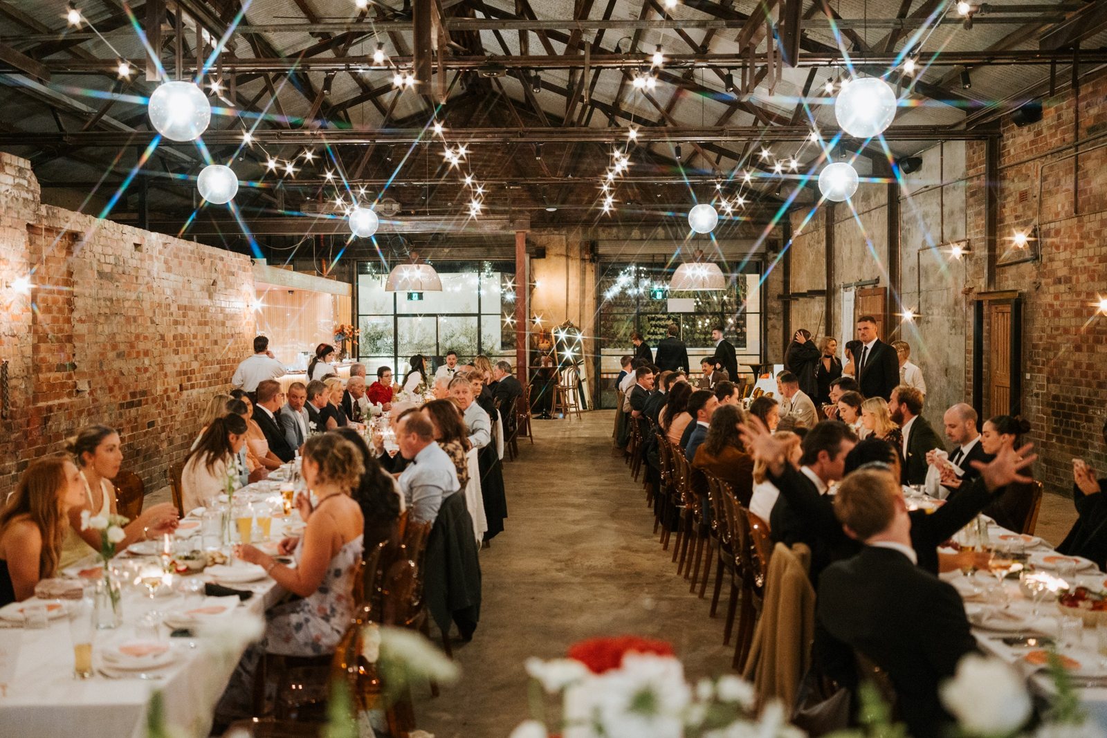 Guests at long tables under globe lights in the Truck Room